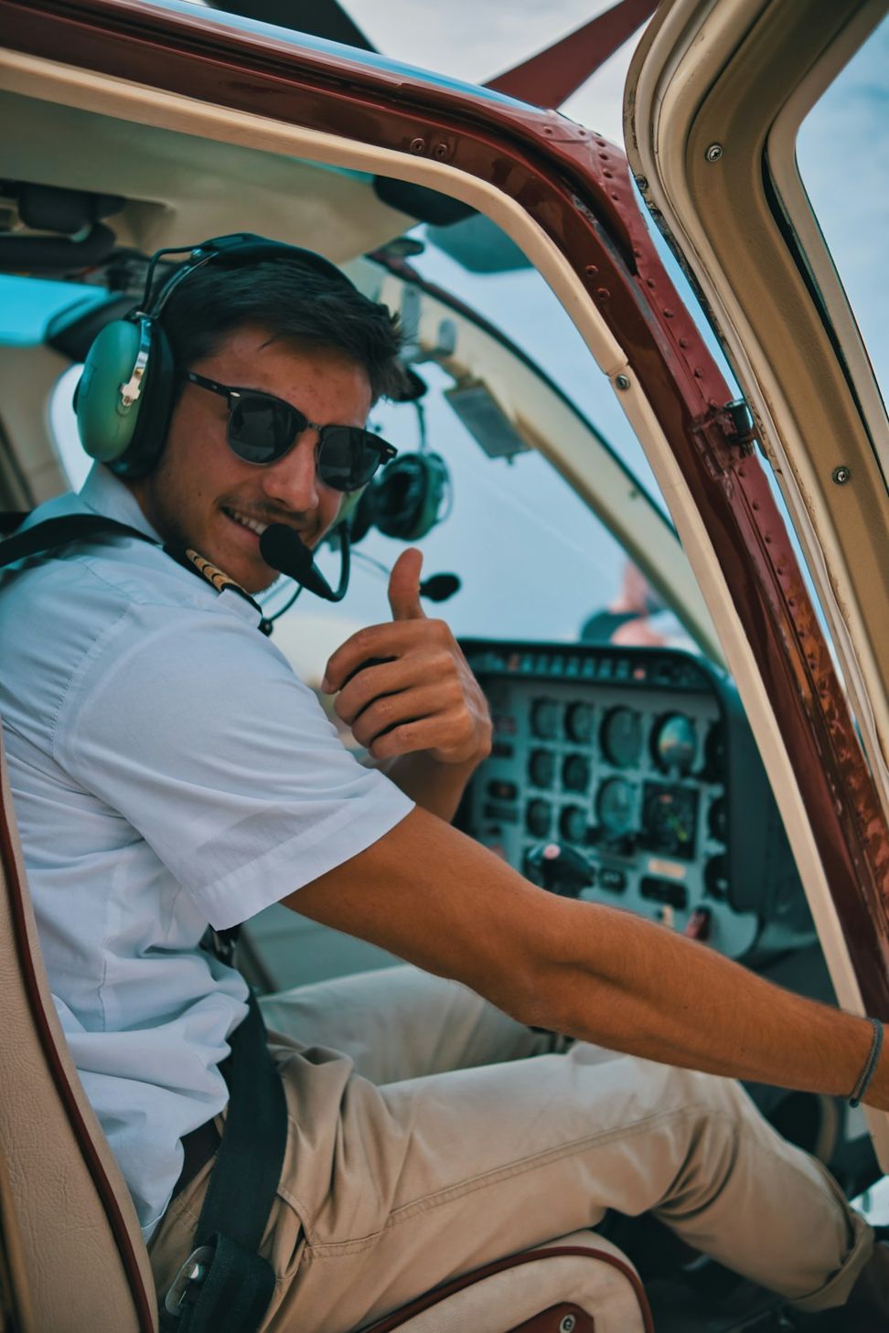 Piloto de óculos escuros e fone sorrindo na cabine de um helicóptero