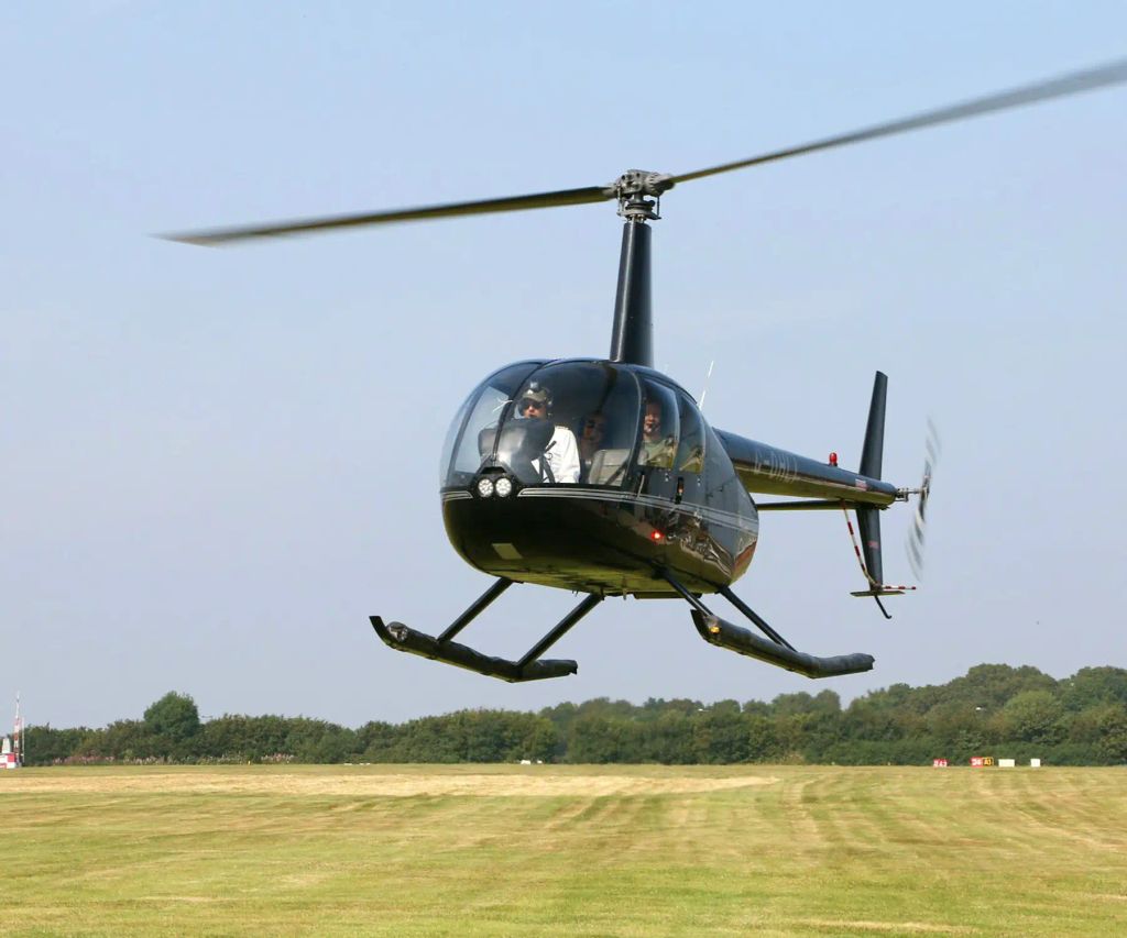Helicóptero preto pousando sobre o gramado do heliponto, com árvores ao fundo