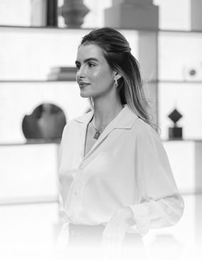 Vera Teixeira em pé diante de uma janela, de camisa branca