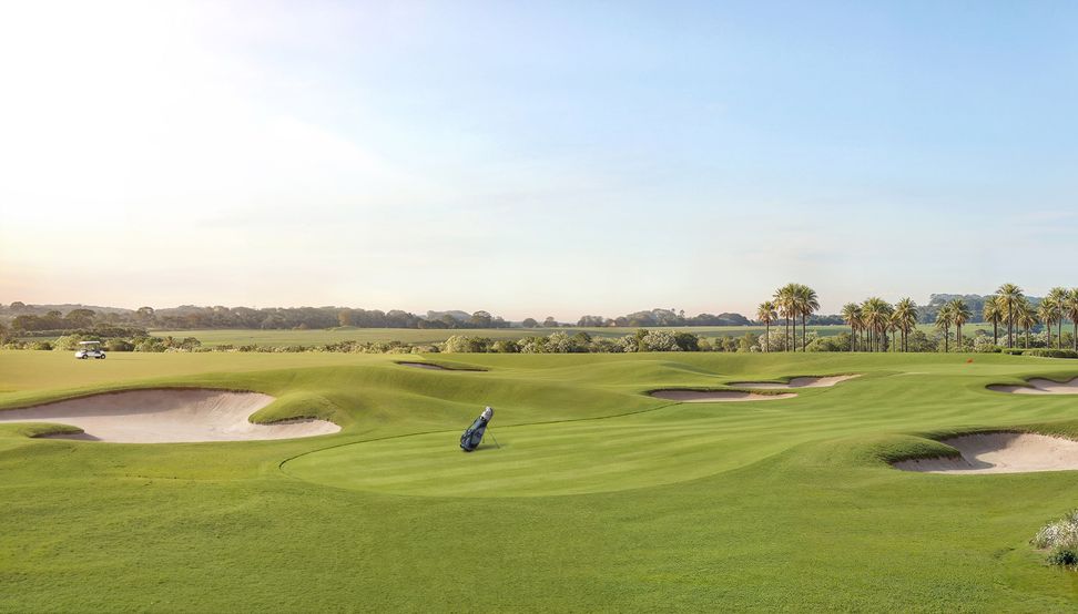 Vista do campo de golfe com bunkers de areia clara e o arvoredo no horizonte