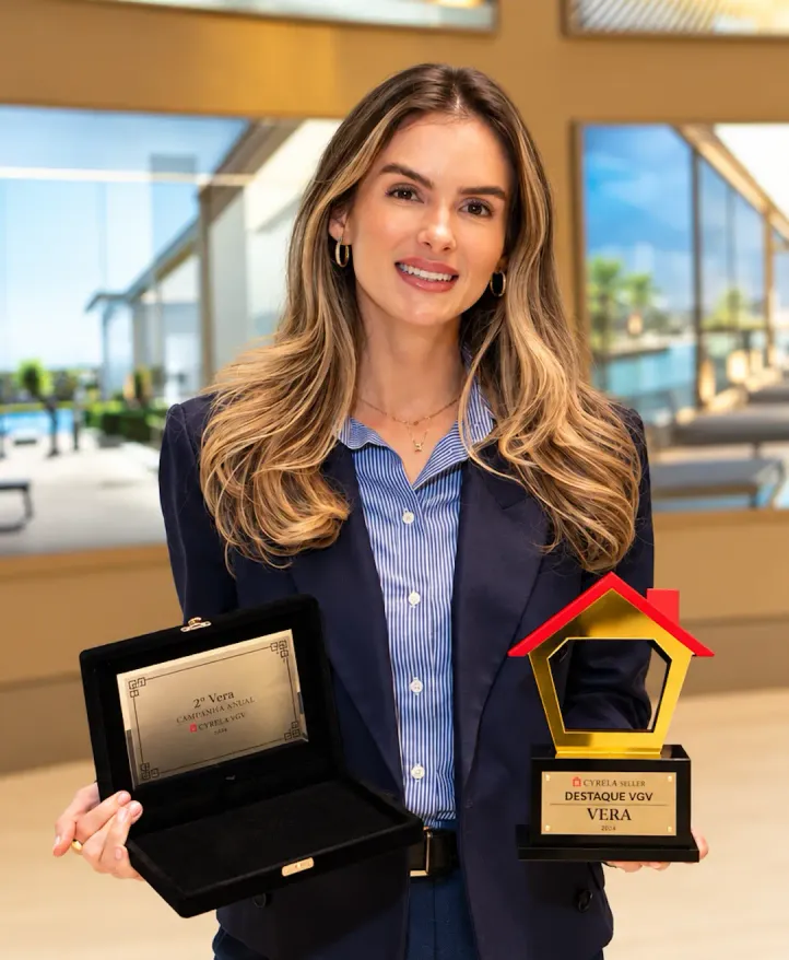 Vera Teixeira sonriendo, con blazer azul marino, con dos premios en las manos